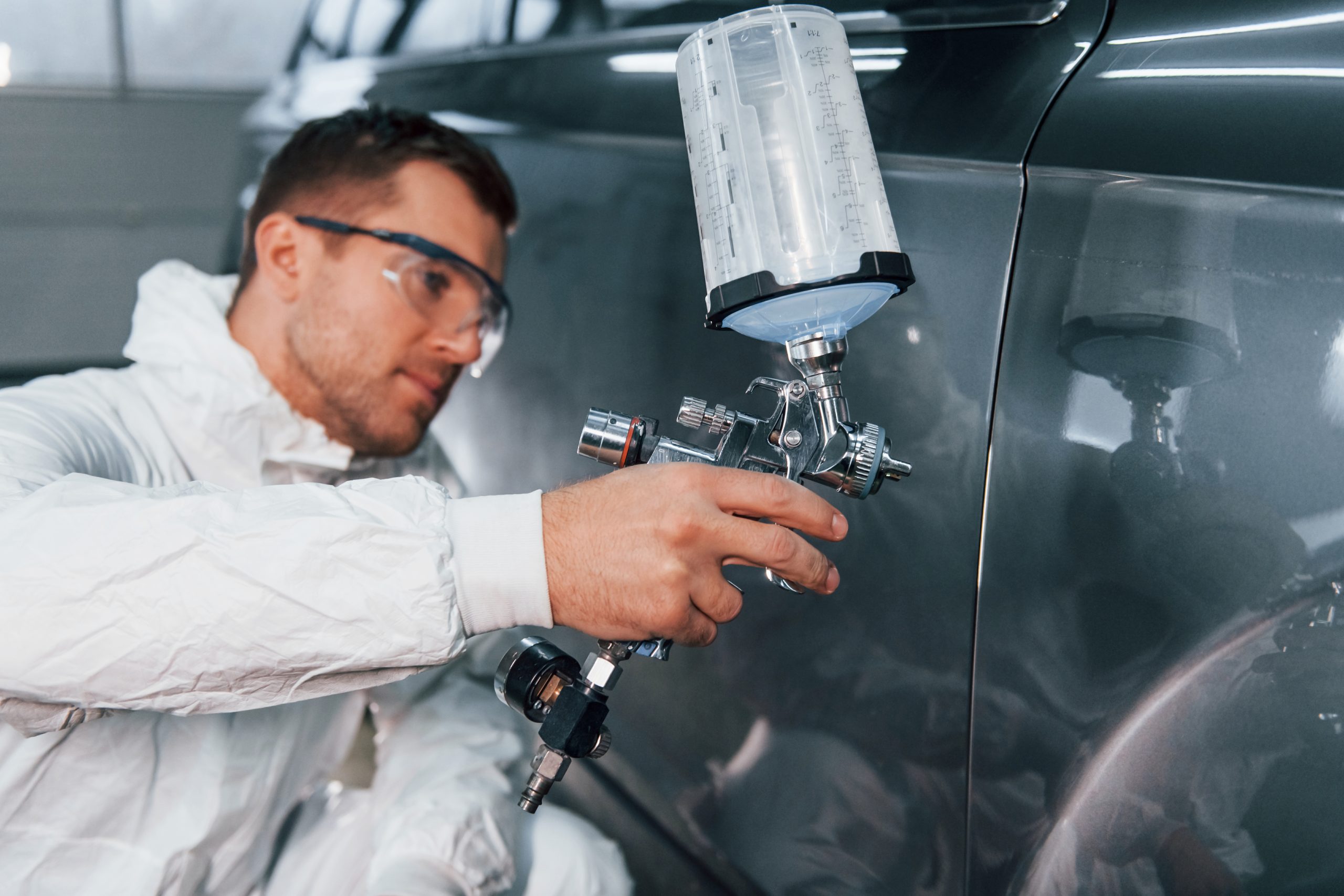 Process of painting the car. Man in uniform is working in the auto service