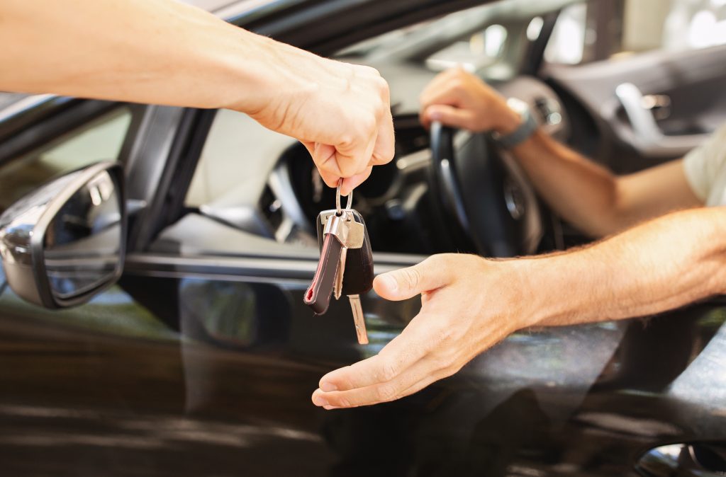 Valet parking worker giving key to man sitting in car